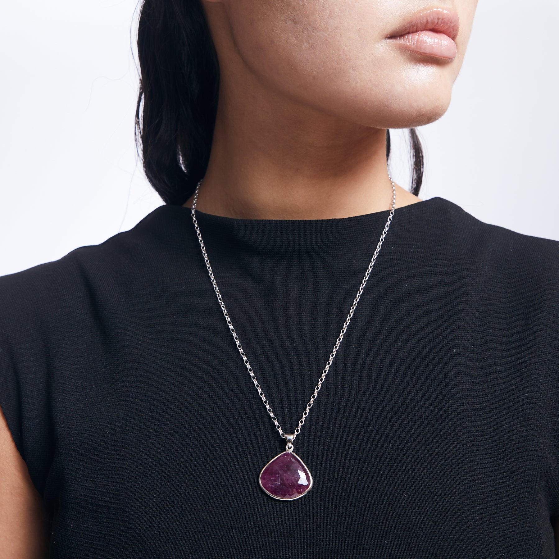 Ruby teardrop pendant with checkerboard faceted finish on sterling silver chain on model